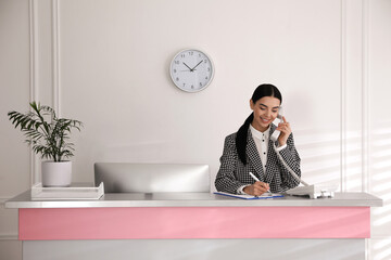 Receptionist talking on phone at countertop in office