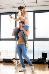 Fototapeta premium Couple caucasian man and woman play the game console with VR glasses at home, man holding wife on shoulders. Excited people having fun with new trends technology. Gaming concept. Video game