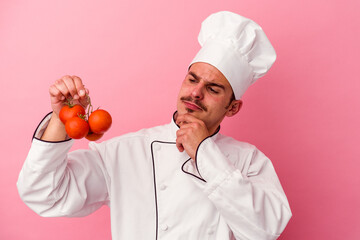 Young caucasian chef man holding tomatoes isolated on pink background