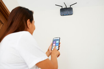 Housewife setting wi-fi router hanging on wall via application on smartphone