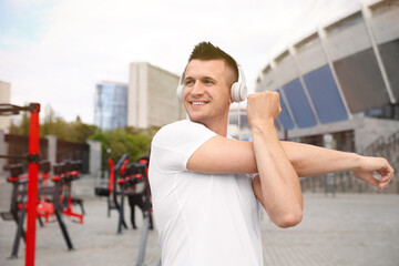 Fototapeta premium Man with headphones stretching before morning fitness near outdoor gym