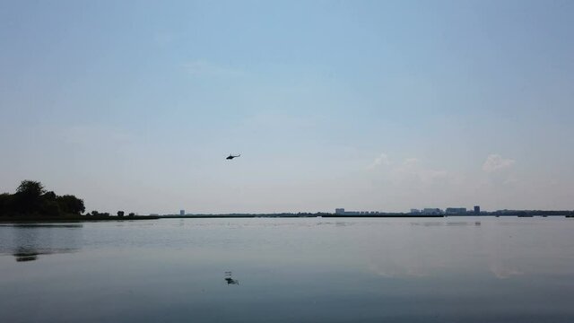 military helicopter flies over the river reflecting in the water