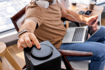 Cropped male use Smart audio speaker. voice assistant helper at home used by young guy. male sits with laptop, turn on modern technology innovation device. copy space. focus on device