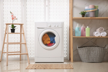 Modern washing machine with clothes in bathroom