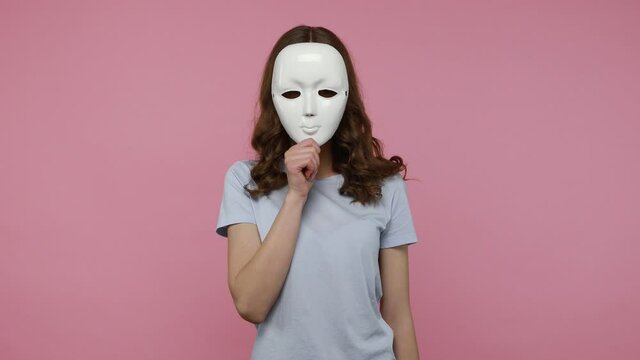 Multiple personality. Attractive teenager girl wearing casual T-shirt showing different emotions, taking off mask changing facial expressions. Indoor studio shot isolated over pink background.