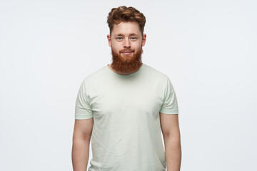 Obraz premium young confident redhead male, watching at the camera, smiling while posing in studio. isolated over white background.