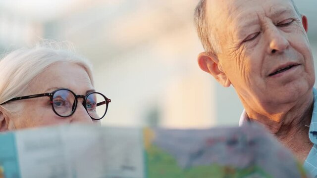 A Good Looking Elderly Tourists Couple Man And Woman Are Looking Map While Walking In The City