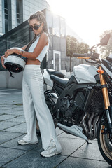 Woman holding helmet posing around motorbike on sidewalk