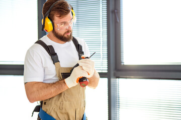 Focused Handyman In Safety Glasses and Overall, Hold Electric Power Tool In Hands, Going To Repair House, Looking Serious. Side View