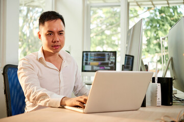 Fototapeta premium Serious frowning software developer working on laptop at his office desk