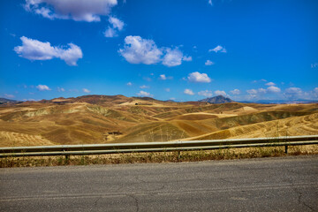 a road runs through the landscape in the summer of the pastures of central sicily