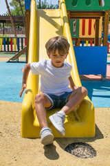 Fototapeta na wymiar Child Playing In The Outdoor Playground. Children Play At School Or Kindergarten. Active 6 Year Old Caucasian Boy With Colorful Slides And Swings. Healthy Summer Activities For Children.