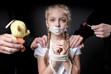 Child abuse. Abduction of children. Slavery and the sale of people. Psychological violence.Scared caucasian little girl is afraid of man in black, kidnapping her. Isolated on black studio background - obrazy, fototapety, plakaty