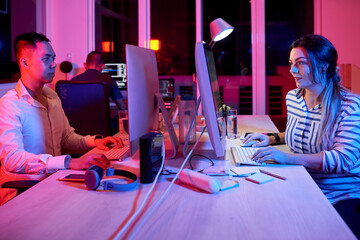 Team of software developers working on big project late at night in neon light trying to finish...