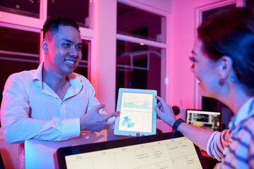 Positive entrepreneurs discussing diagram on tablet computer showing good sales when working in...