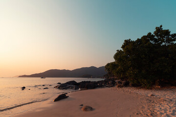The South China Sea beach and trees in front of a mountain against a sky at spring sunset