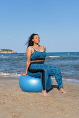 Fototapeta na wymiar Woman practicing yoga fitness exercises using fitness ball on beach
