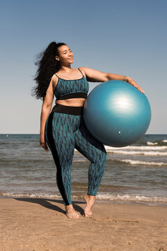 Woman holding a fitness ball doing yoga or pilates exercises on beach