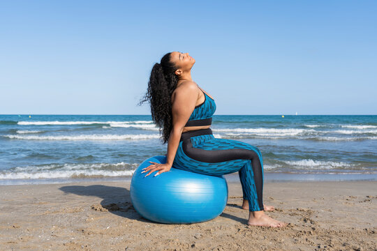 Woman practicing yoga fitness exercises using fitness ball on beach