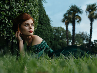 pretty woman in green dress lies on the grass in the fantasy garden