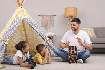Father and children playing near toy wigwam at home © New Africa