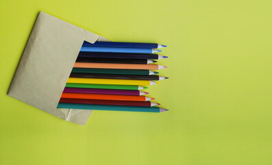Colored, wooden pencils in an envelope on a yellow background. School supplies and stationery, preparation for school. Education concept. Place for your text.