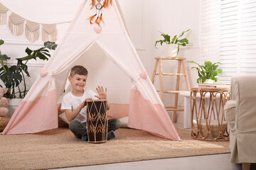 Cute little boy playing drum near toy wigwam at home © New Africa