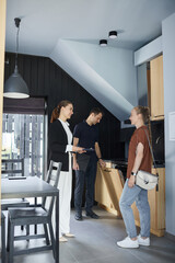 Fototapeta premium Vertical full length portrait of smiling real estate agent showing house to young couple buying property