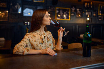 Young woman drinks red wine at the counter in bar