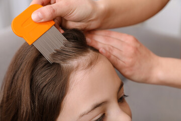 Mother using nit comb on her daughter's hair indoors. Anti lice treatment