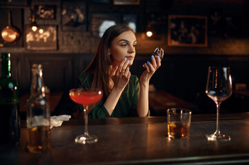 Depressed woman drinks alcohol at counter in bar