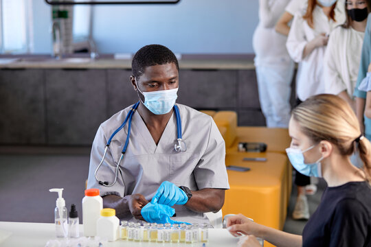 Vaccination against coronavirus. Mass vaccination. Male black doctor preparing to inject the flu, pneumonia, or COVID-19 vaccine into the patient's shoulder, side view