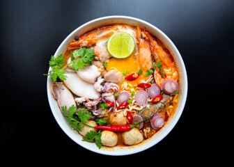 Hot and spicy noodle soup in white bowl on black background.