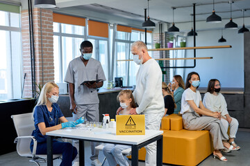 Doctors and medical staff in vaccination rooms for corona virus, covid 19, caucasian people sit waiting for recieving vaccine. Mass vaccination. female doctor doing injection to patient child