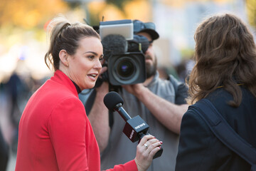Shallow focus of an adult female news reporter broadcasting from a climate change protest outdoors