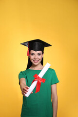 Happy student with graduation hat and diploma on yellow background