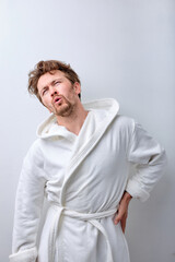 people person concept. portrait of sad upset man feeling pain in back on white studio background. Bearded caucasian guy in bathrobe suffer from pain in spine back. copy space for advertisement