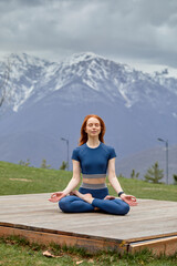 Naklejka na ściany i meble Adorable young woman sitting outdoors in yoga position and meditating with closed eyes in nature. Peaceful female enjoy rest, relax in tranquility. side view portrait