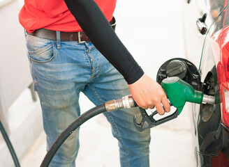 Asian gas station worker man catching green fuel nozzle into one hand while filling high energy...