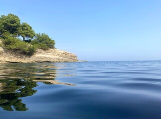 Obraz premium Beautiful Adriatic sea. island in coastal rocks covered pine trees. Blue clear glittering water surface. Summer. Relax. Tranquility. Awesome nature of Mediterranean coast. Horizon over calm water.