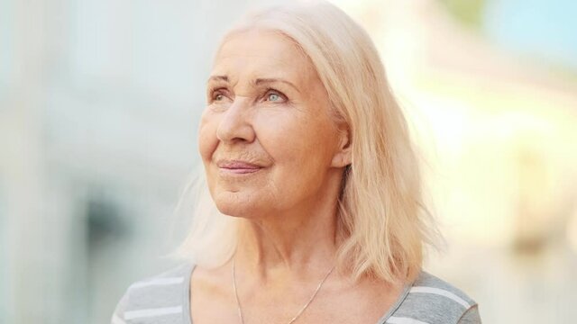 A blonde elderly woman is looking sights while walking outside on the street