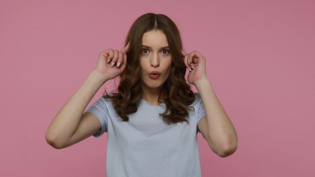 You are fool. Displeased teenager girl in casual style clothing looking with indignant expression, twisting finger near temple, showing stupid gesture. Indoor studio shot isolated over pink background