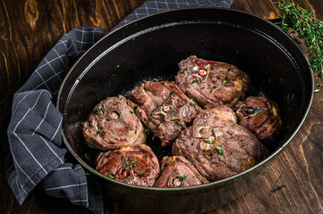 Stewed lamb neck meat in a pan with herbs. wooden background. Top view