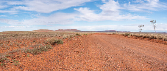 Unsealed Outback road, remote travel. Ultra wide panorama, South Australian landscape. Dirt  road access to remote Outback communities and Stations.