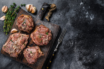 Grilled lamb neck meat steaks on a wooden board with herbs. Black background. Top view. Copy space