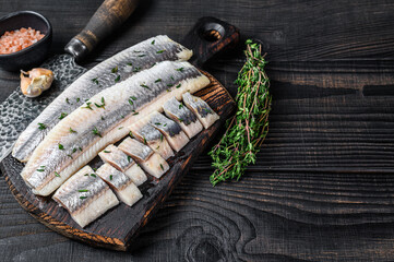 Sliced salted herring fish fillet on a wooden board. Black wooden background. Top view. Copy space
