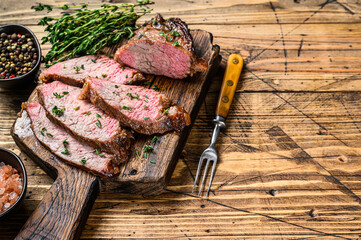 Rare slices of Roast beef sirloin tri tip steak bbq on a wooden cutting board. wooden background....