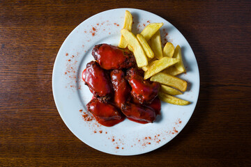 plate with chicken wings in barbecue sauce and french fries over wooden table. view from top
