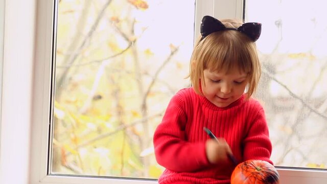 Cute Little Girl painting pumpkin for halloween and singing at home. Autumn activity for children concept