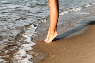 Children's feet on the sand by the sea. The child stands on her toes near the sea waves on the sand